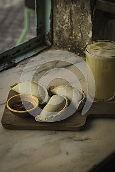 Small chopping board displaying typical food from Portugal and South America, Chicken and Beef Empanada favored with spicy and