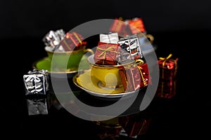 Small christmas gift packs over colorful cups on black background