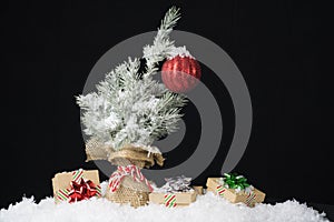 Small Christmas tree with one red ornament wrapped in burlap covered in snow with three simple presents beneath