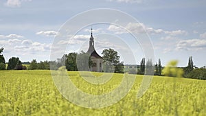 Small church, baroque chapel with belfry at field with oilseed rape