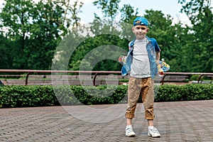 A small city boy and a skateboard. A young guy is standing in the park and holding a skateboard. City Style. City children. A