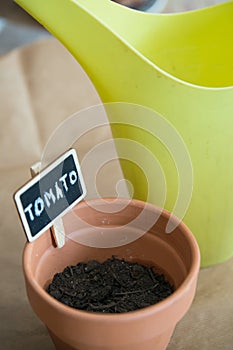 Small clay pot with tomato seeds to germinate. Watering can behind