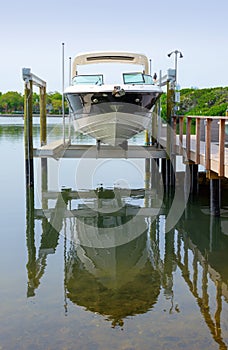 Small clean v-bottom bay motorboat on an electric lift on a wood dock