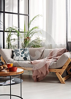 Coffee table in front of scandinavian futon sofa with patterned pillow and patel pink blanket photo