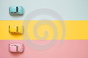 Small color toy cars at the start on a yellow, pink and blue background. Racing cars on a table top racetrack