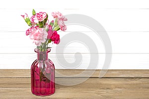 Small colored pink carnations in a vase on wooden background and white wall Hello spring, seasonal concept Mock up Place for text