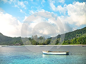 Small colorful boat anchored off a Seychelles beach with distant