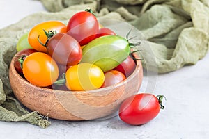 Small colorful cherry tomatoes in wooden bowl on table, horizontal