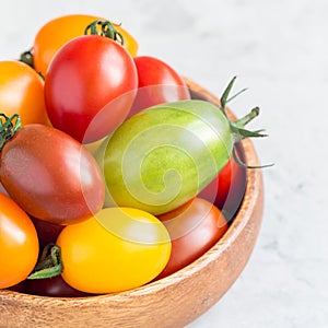 Small colorful cherry tomatoes in wooden bowl on a table, square