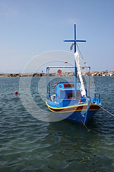 Small colorful fishing boat boat moored in Crete with mast and furled sail