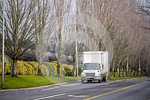 Small compact rig truck with box trailer transporting local goods on the city road with tree alley and railroad