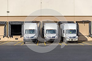 Small compact rigs semi trucks with box trailers standing in row at warehouse docks for loading cargo