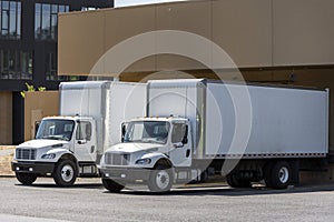 Small compact rigs semi trucks with long box trailers standing in warehouse dock loading cargo for delivery