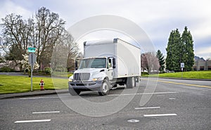 Small compact semi truck with cube box trailer transporting commercial cargo driving on the street of urban city in spring time