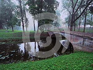 Small concrete old bridge over a small river in a town forest park in a fog. Mistry surreal calm mood. Relaxing atmosphere and