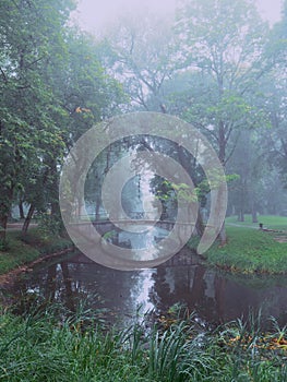 Small concrete old bridge over a small river in a town forest park in a fog. Mistry surreal calm mood. Relaxing atmosphere and