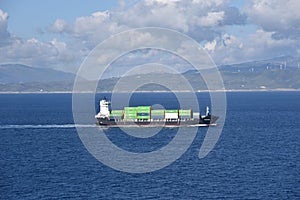Small container ship sailing near sea coast close to Gibraltar.