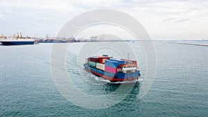 Small container ship sailing in sea and shipping port background aerial view