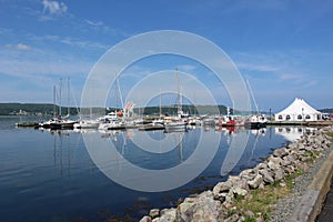 A small convention tent set up at a marina in the Strait of Canso with yachts along a seawall on a calm warm sunny day