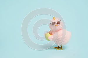 small cool chick in sunglasses with Easter egg on blue background, copy space