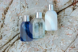 Small cosmetic bottles - shampoo, shower gel, lotion on beige stone background.