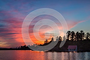 Small cottage in shadow on a lake at sunset.