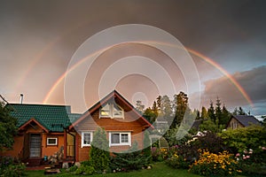 Small country house on a summer evening. Rainbow over the house. Beautiful sunset. Flowers in the garden