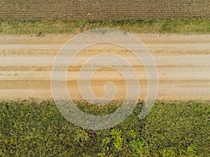 Small country road and freshly ploughed soil on one side and green meadow on the other. Aerial view