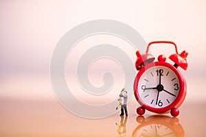 Small couple figures in love and red alarm clock.