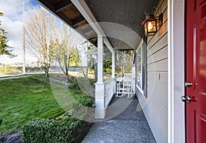 Small covered porch with white rocking chair and red front door.