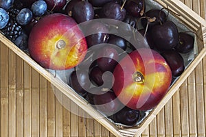 Small crate with flat nectarines, cherries, blueberries and blackberries.