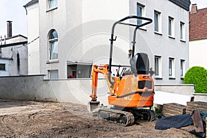 Small crawler excavator at a construction site near a residential building.