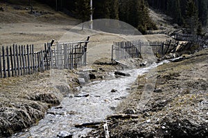 Small creek against the old wooden fence, in forest.