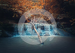 Small creek waterfall with water falling through the autumn woods. Fast stream flowing down from the spring in the forest, through