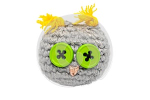 Small crocheted owl toy of gray threads with yellow ears, a pink nose and eyes of green buttons isolated on a white background