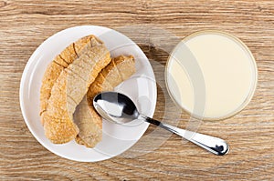 Small croissants in saucer, spoon, bowl with condensed milk on table. Top view