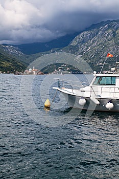 Small cruise boat for transfer to island of Gospa od Skrpjela moored in Perast city marina. Islet is on background. The Kotor bay