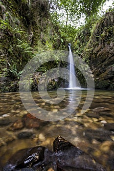 A small crystalline waterfall in a lush forest, long exposure with wet rocks in the foreground and silk effect, Chorron waterfall