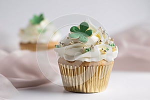 Small cupcake with cream and gold beads and a green clover on a light background. Green four-leaf clover symbol of St. Patr photo