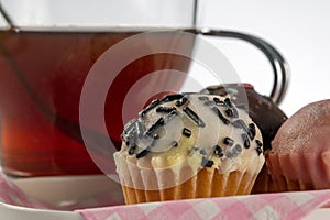 Small cupcakes on a tray with a pink checkered napkin, accompanied by a glass of tea