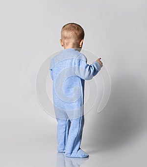 Small cute baby boy in blue warm comfortable jumpsuit standing and keeping balance, rear view