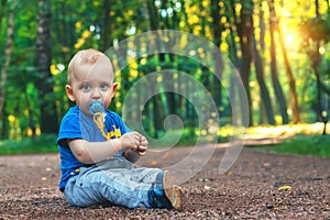Small cute baby with nipple sits on the footpath in the dreamlike forest all alone. Little boy sitting on the ground.