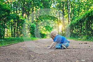 Small cute baby with nipple sits on the footpath in the dreamlike forest all alone. Little boy sitting on the ground.