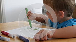 Small cute boy drawings colored pencils on a sheet of paper