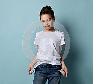 Small cute boy with modern hairstyle in stylish casual clothing standing and showing empty pockets, copy space