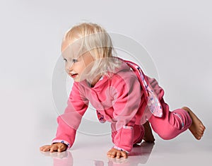 Small cute cheerful blonde baby girl in pink warm comfortable jumpsuit crawling on floor