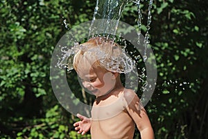 Small cute child is poured with cold water from bucket. Water games on hot summer day in backyard. Hardening for health.