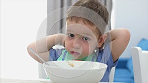 Small Cute Child is Sitting at a Table and eat his own oatmeal, the baby eats willingly. Concept Happy Childhood.