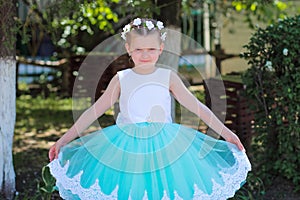 Small cute girl in a blue and white dress and wreath raises the hem of her dress