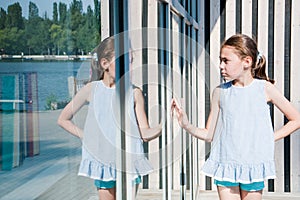 Small cute girl looks at her reflection sunny day